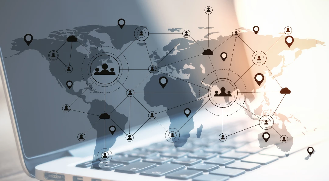 Graphic of a world map overlaid with connected pin and people icons on a laptop keyboard, illustrating a global remote workforce network.