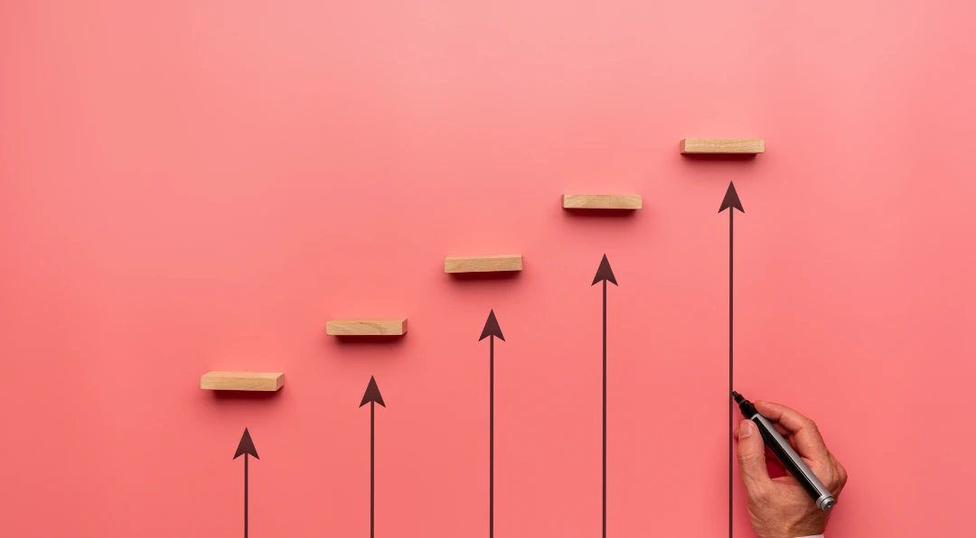 Illustration of a hand drawing an upward staircase of wooden blocks with rising arrows on a pink background.