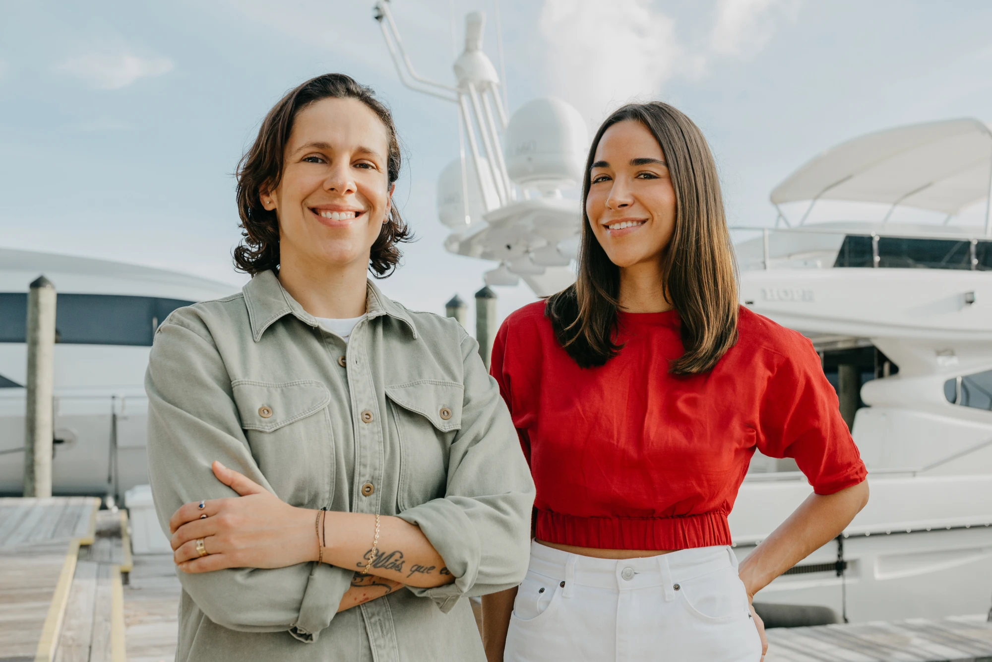 Two smiling women standing together on a dock in front of a large white yacht.