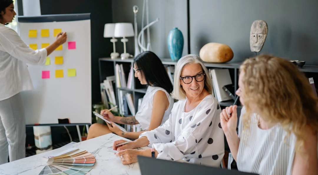 A person's hands holding a printed business dashboard with pie charts and bar graphs, next to a smartphone showing the same charts and an open laptop.